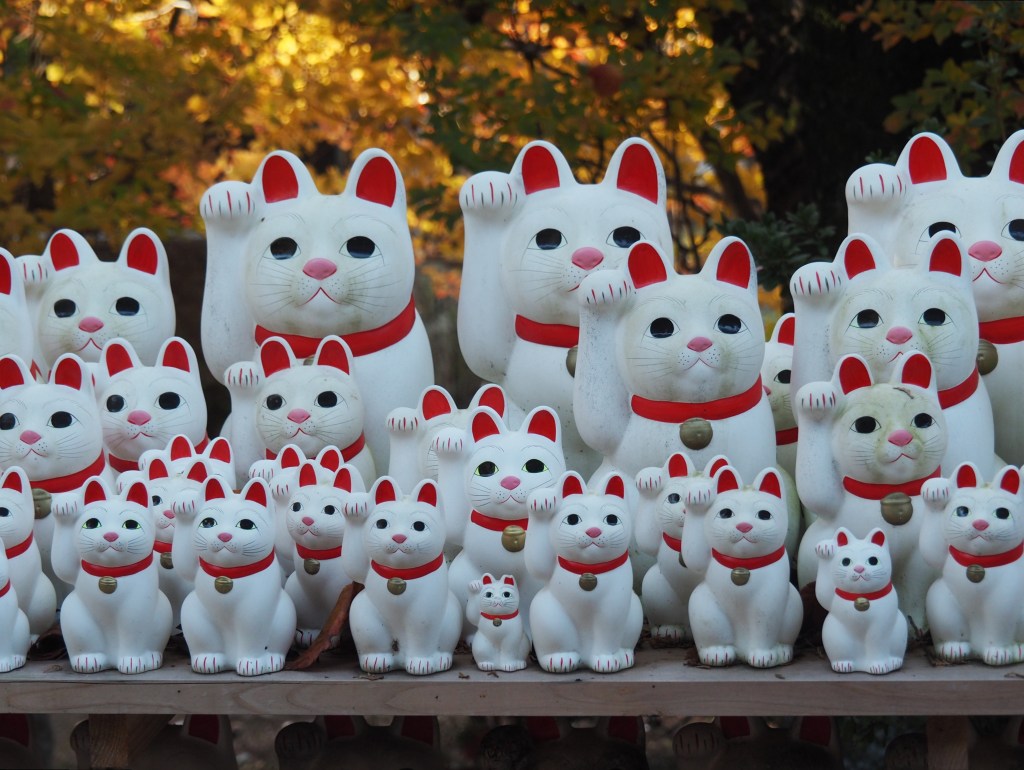 Maneki-neko figurines at Gotoku-ji, Tokyo. By Laika ac from UK, at WIkipedia (CC BY-SA 2.0)